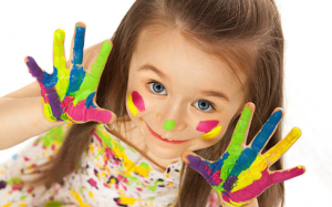 Niña con las manos pintadas de colores brillantes durante una fiesta infantil, representando creatividad y diversión inclusiva.